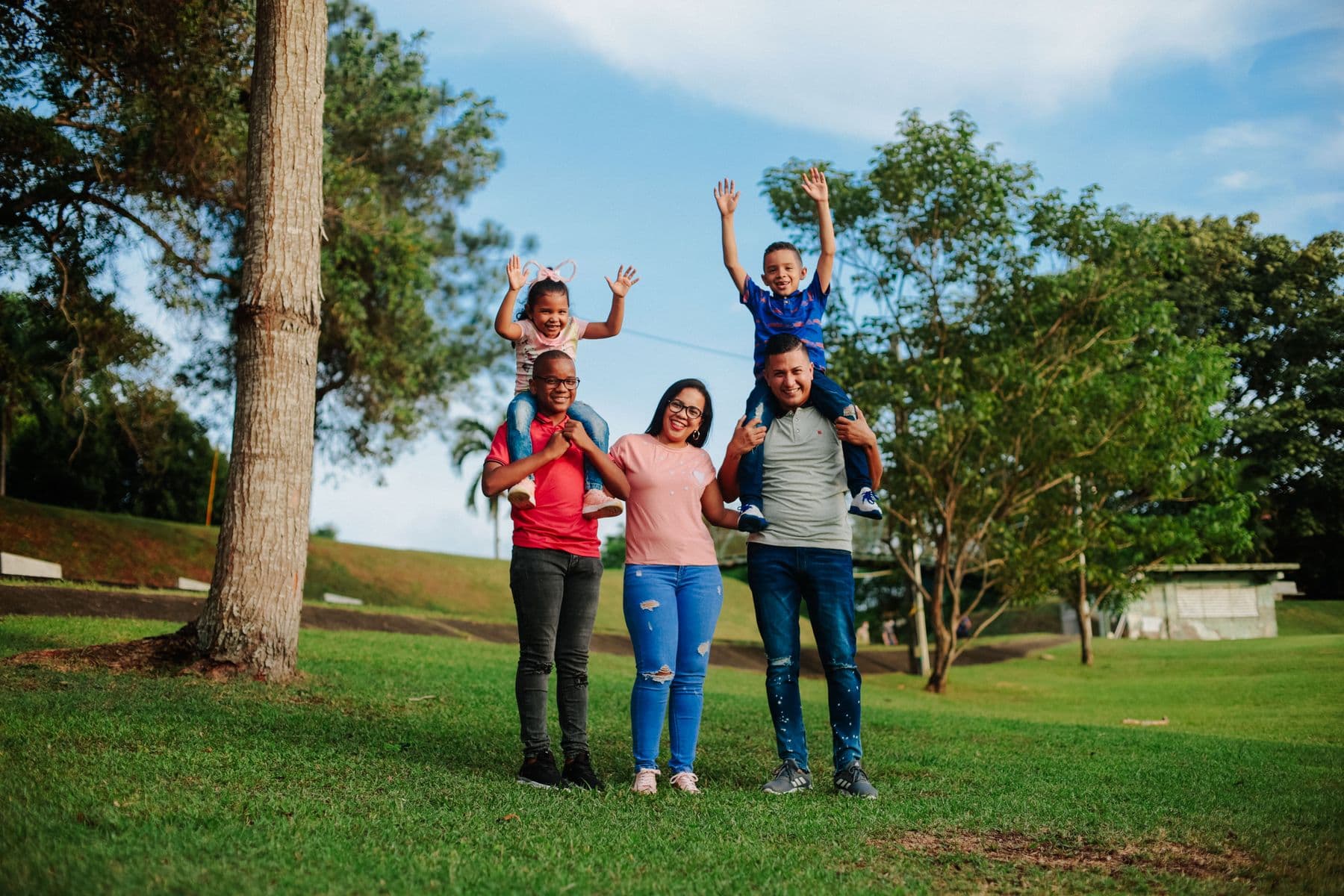 A happy family of four smiling together outdoors on a sunny day
